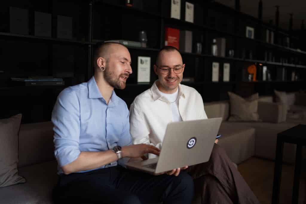 Troi Meetingfoto: Zwei Personen arbeiten gemeinsam am Laptop mit Troi-Logo, entspannt im Gespräch